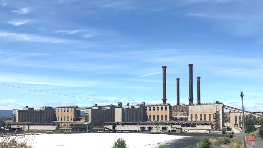 A wide shot of the factory, with four dark black chimneys