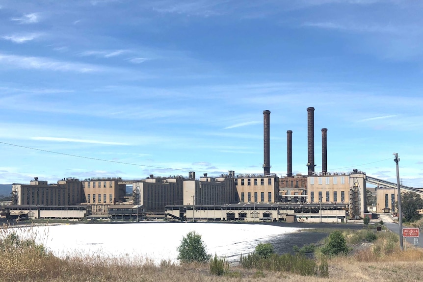 A wide shot of the factory, with four dark black chimneys