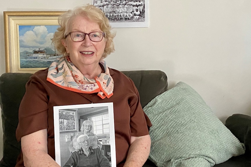 Woman holds photo and sits on couch.
