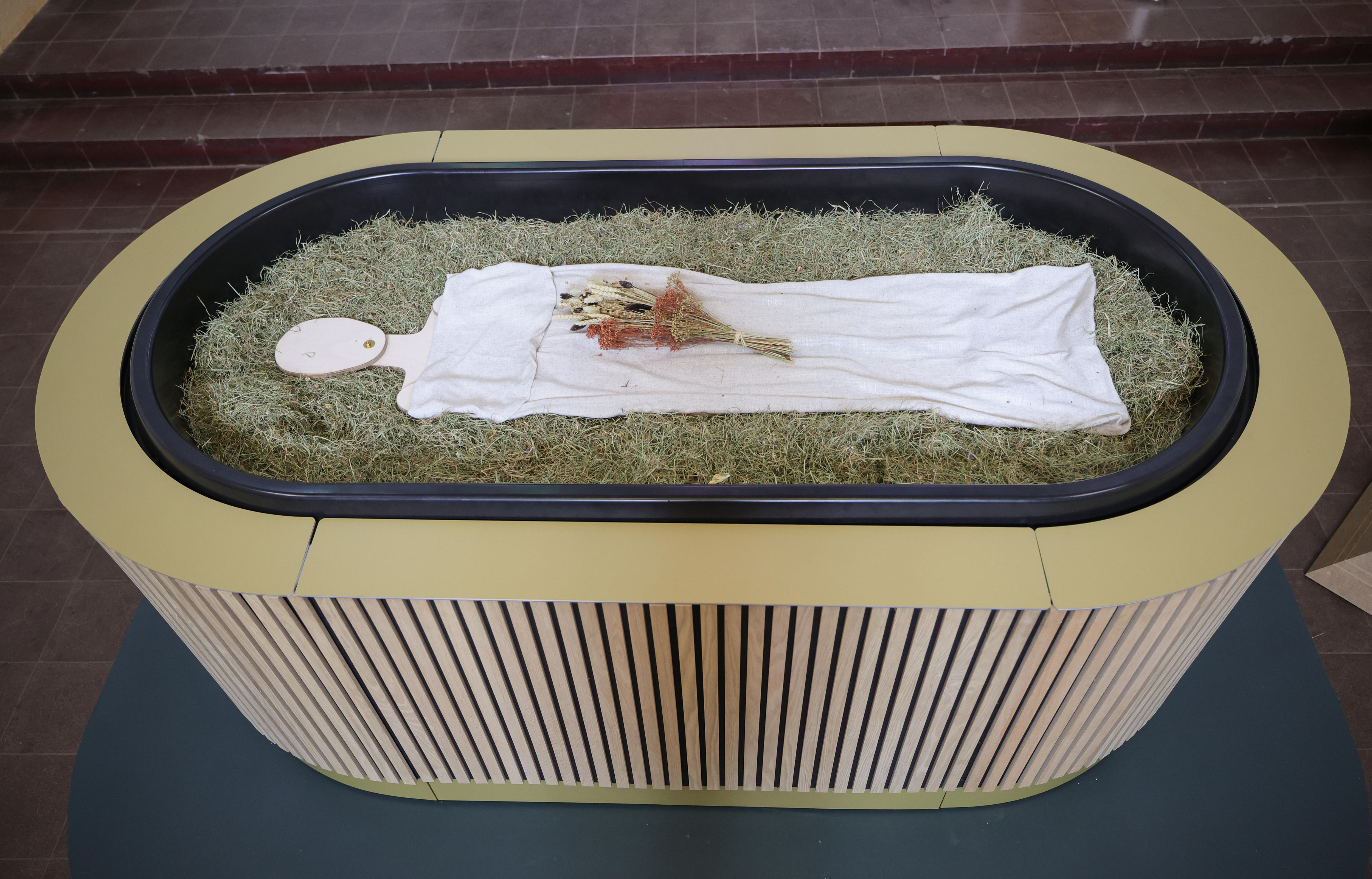 oval shaped tub, filled with matter topped by straw, and a cut out wooden figure lying on top