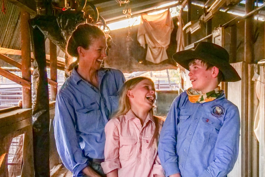 A woman, a boy and a girl standing in a shearing shed laughing.
