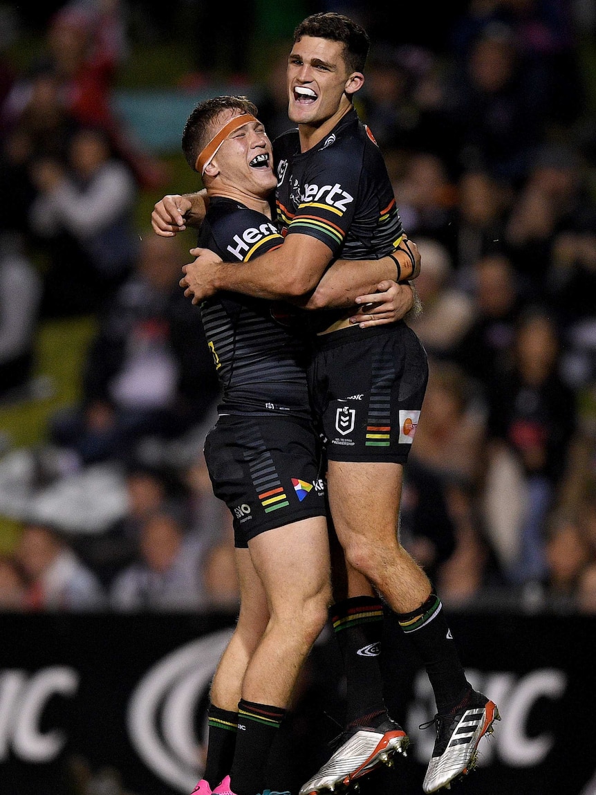 A male NRL player jumps in the air as he is hugged by a teammate as they celebrate scoring a try.