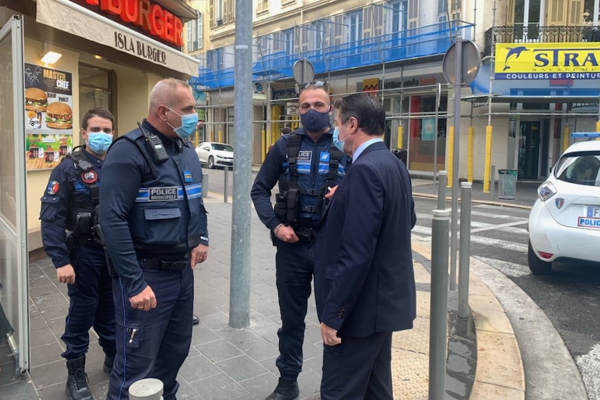 Christian Estrosi stands to the right as he speaks with three police officers in what appears to be the city centre of Nice.