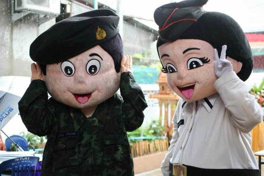 One male mascot wearing Thai military uniform stands next to woman mascot in military uniform doing a peace sign.