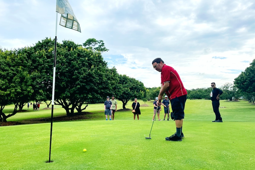 A in a red shirt man putting a golf ball on fine day.