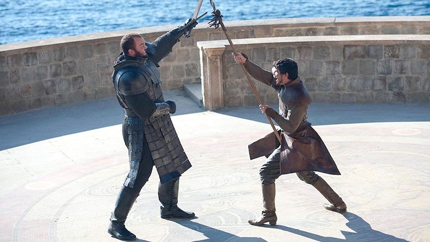 Two armoured men battle with swords and spears in in a scene from a fantasy tv show
