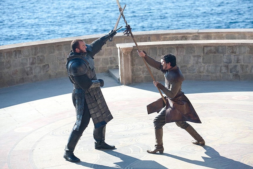 Two armoured men battle with swords and spears in in a scene from a fantasy tv show