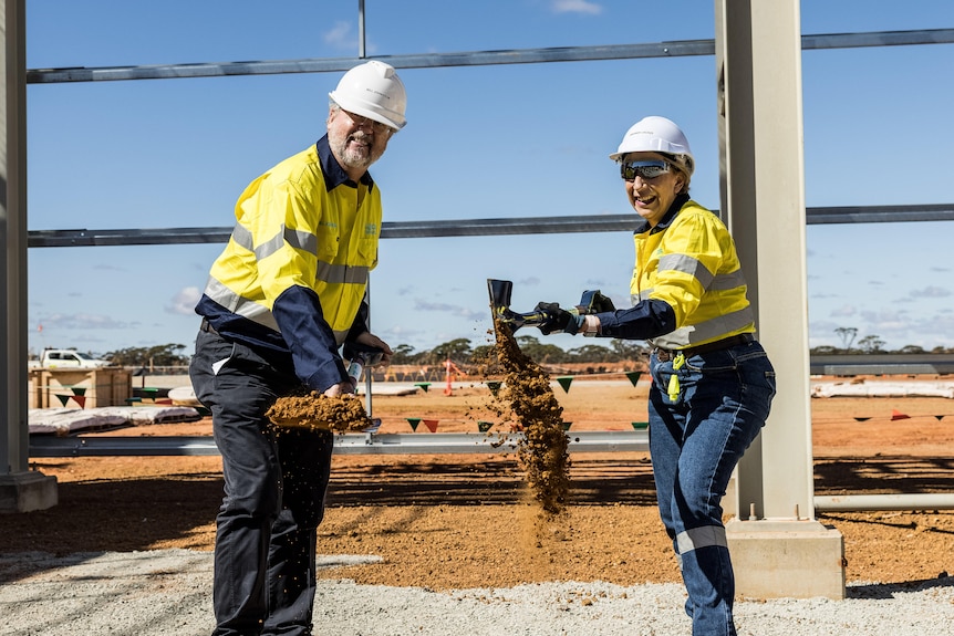 A man and a woman wearing high-vis workwear and hard hats during a ceremony for the turning of the first sod for a new refinery.