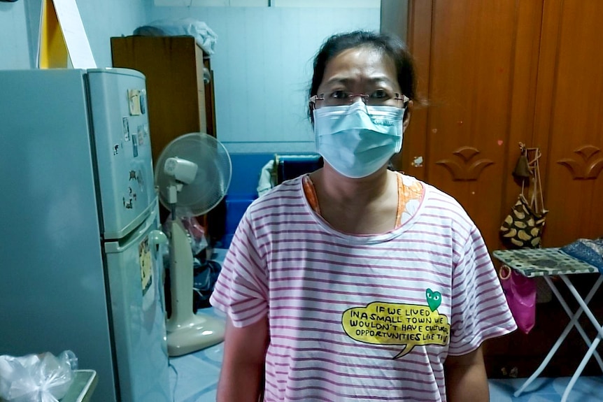 A Thai woman in a striped t-shirt and blue face mask standing in a kitchen 