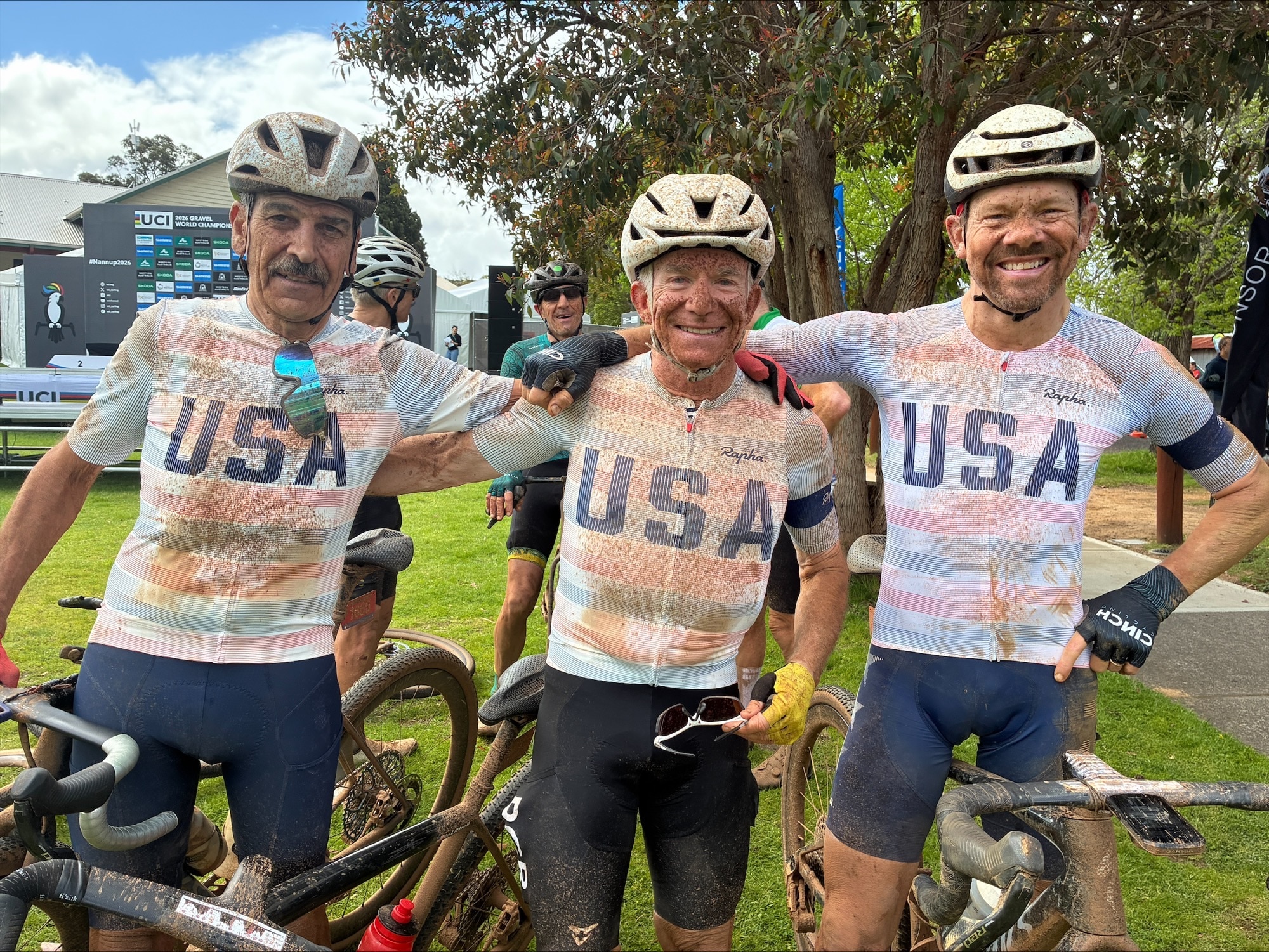The three men are in a row, smiling and wearing white helmets and USA cycling jerseys.