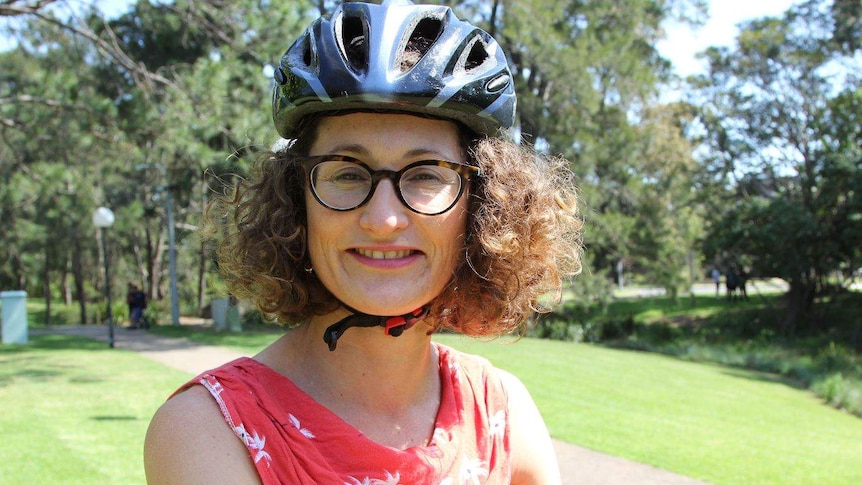 A woman with curly hair, glasses and a bike helmet smiles.