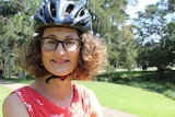 A woman with curly hair, glasses and a bike helmet smiles.