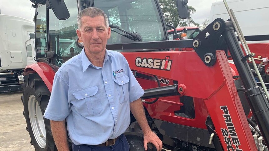Agricultural machinery salesman Ron Arthur stands in front of a tractor