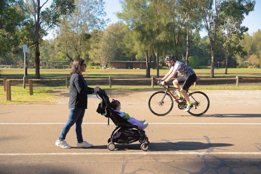 A woman with a baby in a pram and a man on a bike on a footpath.