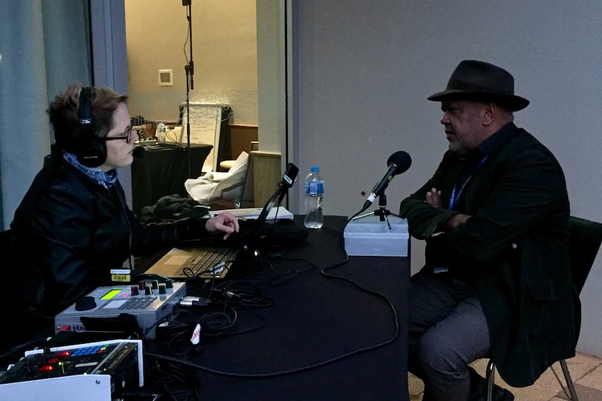 Woman wearing headphones interviewing a man in front of radio microphones.