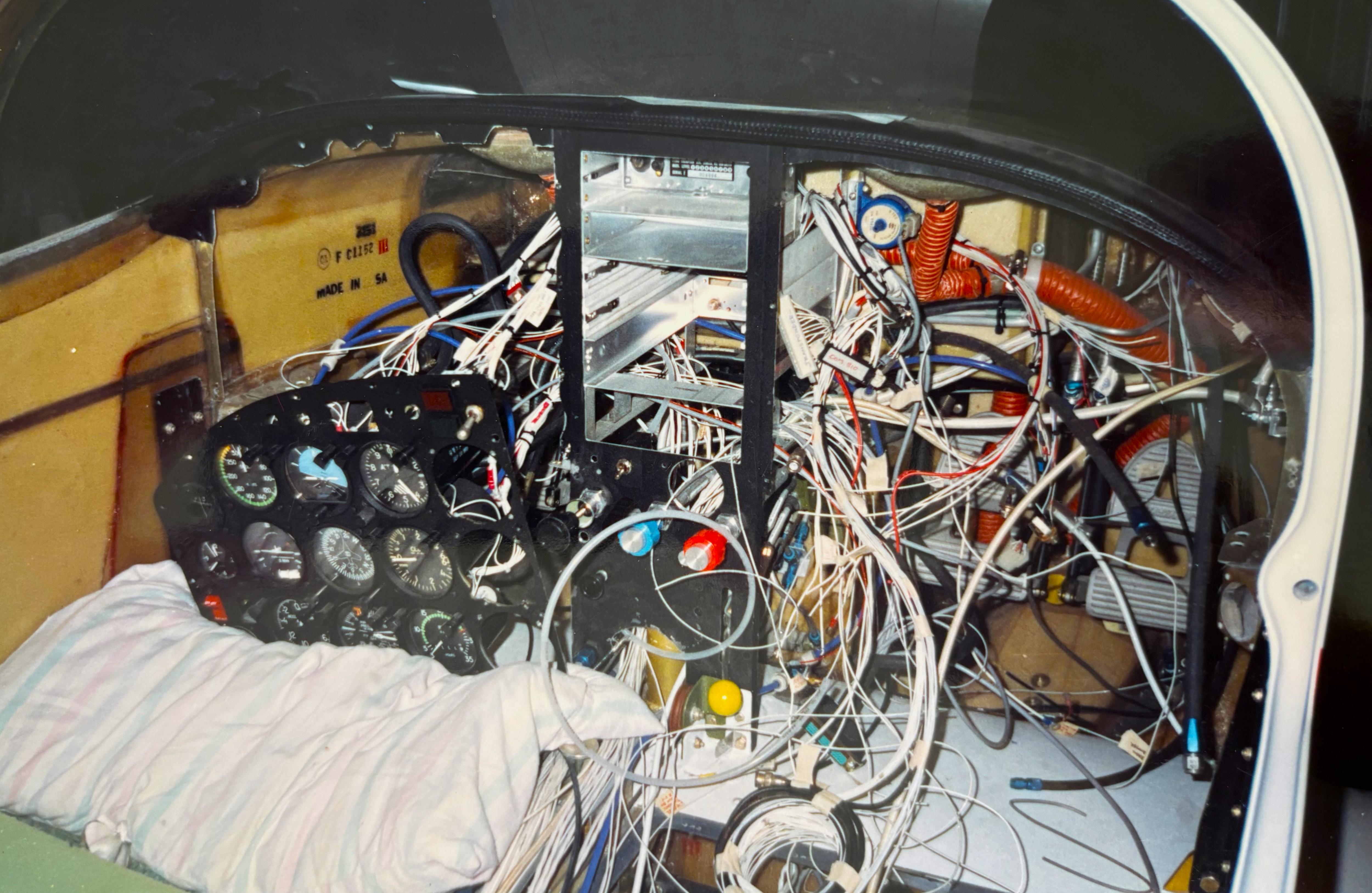 Inside of plane's cabin with view of lots of wires behind instrument panel
