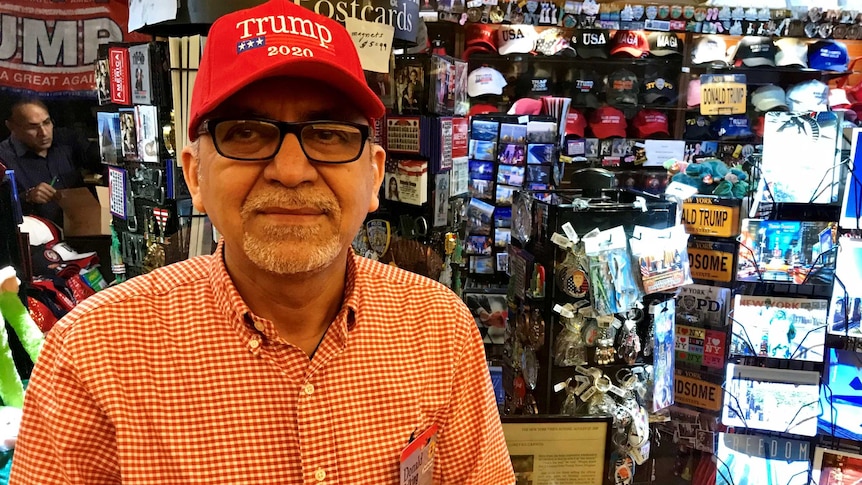 Roger Sewani gives a thumps up to the camera while wearing a Trump hat inside his souvenir store