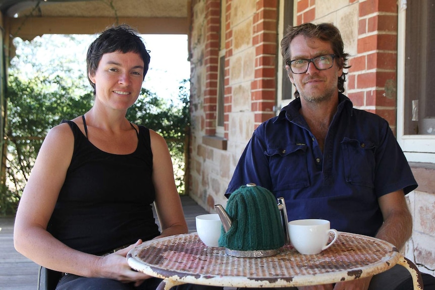 A couple sit together on a porch with tea on the table.