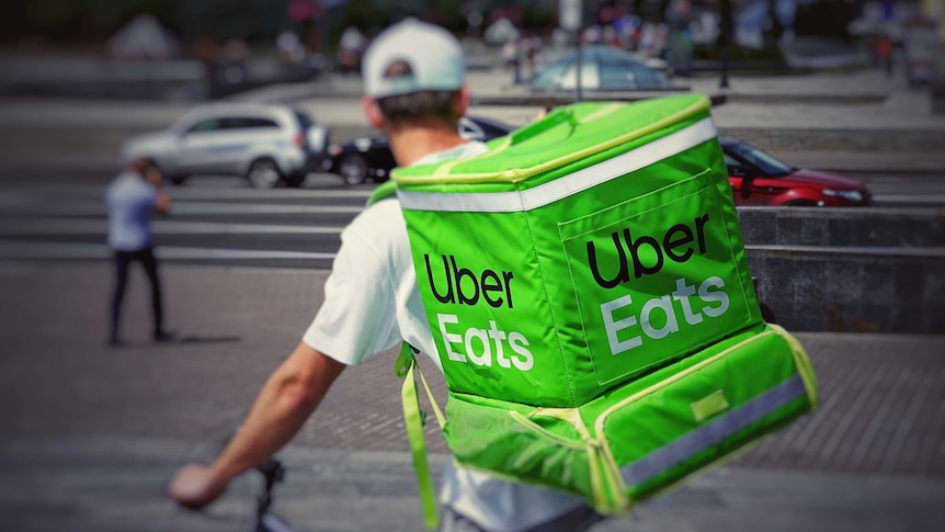 A man on a bike with a green Uber Eats backpack.