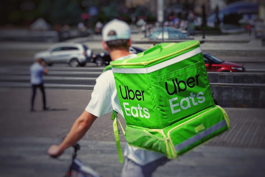 Un hombre en bicicleta con una mochila verde de Uber Eats.