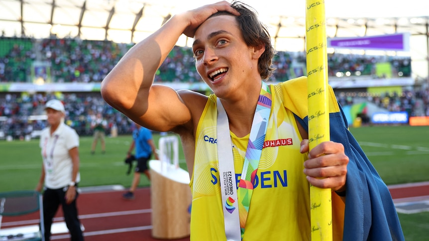 Holding his pole and wearing his gold medal, Armand Duplantis puts his hand to his head and looks shocked
