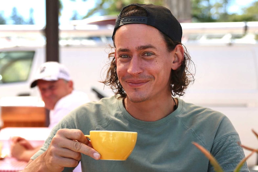 Joseph Andrew, 30, drinks a coffee at cafe table.