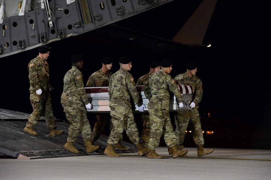 US soldiers carry coffin off plane.