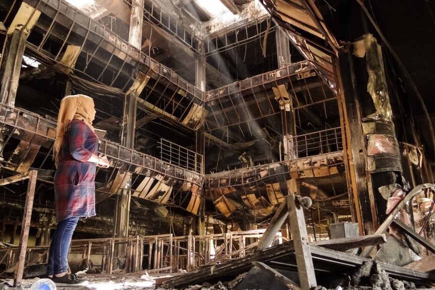 A woman stands in the ruins of Mosul library.