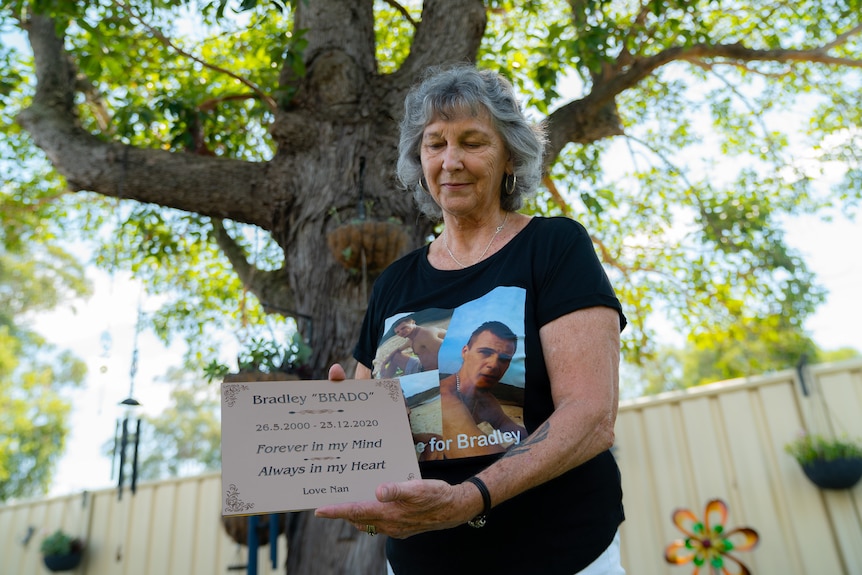 A grandma holding a plaque that reads "Bradley, always in my heart, love nan"