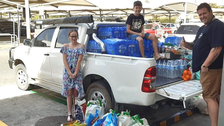 Three people loading a ute with water and supplies at a shopping centre