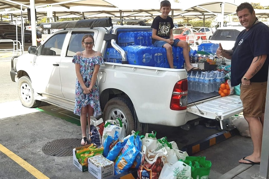 Three people loading a ute with water and supplies at a shopping centre