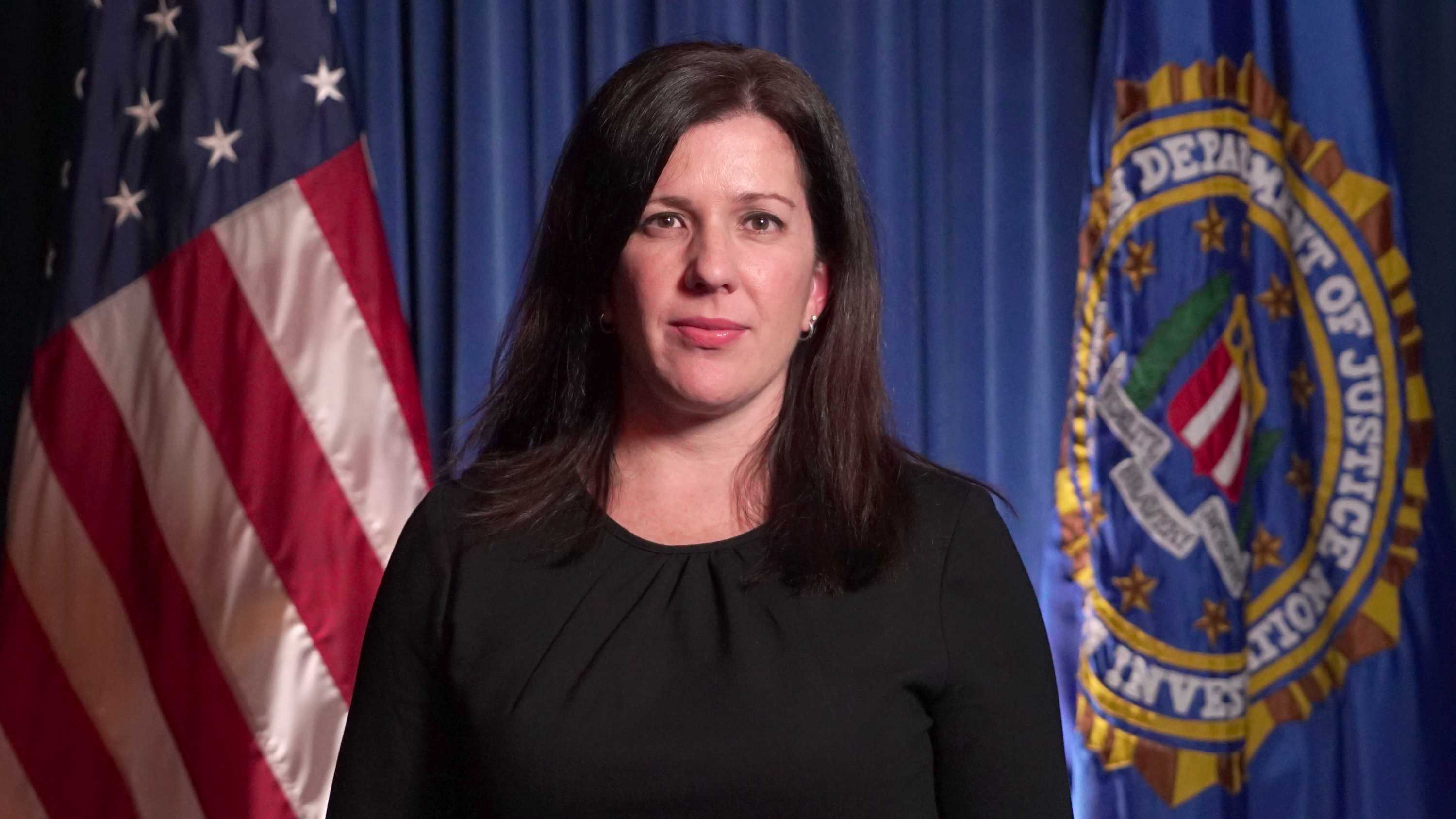 Angela Williamson looks to the camera with a neutral expression on her face with US flag behind her in an official portrait.