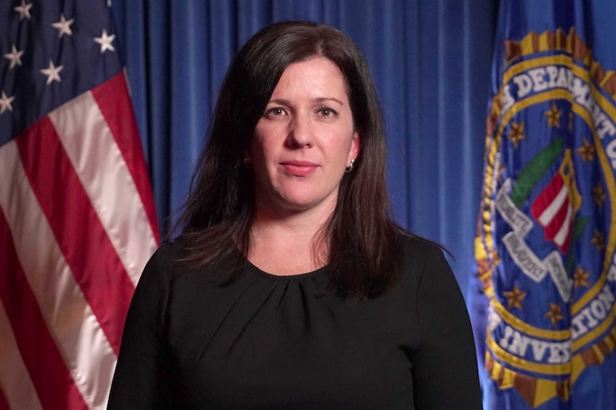 Angela Williamson looks to the camera with a neutral expression on her face with US flag behind her in an official portrait.