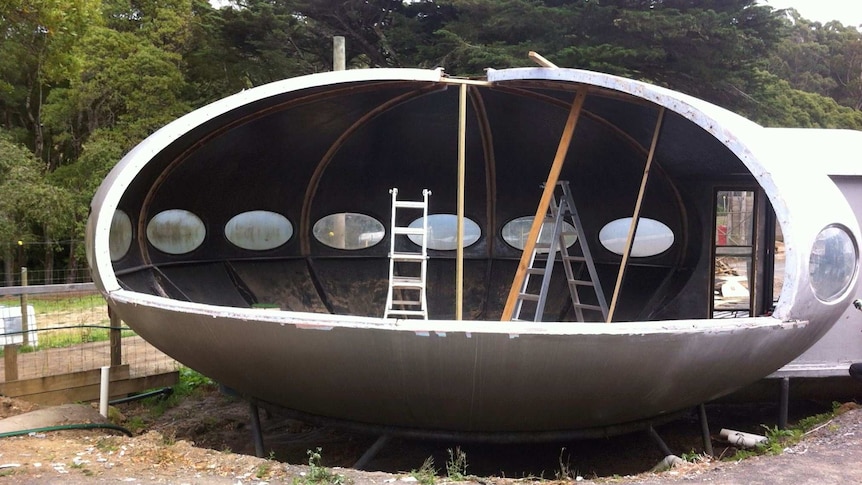 A silver spheroid structure with oval windows, some panels removed revealing the inside.