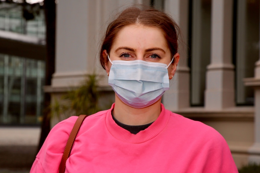 A woman wearing a mask wearing a bright pink jumper