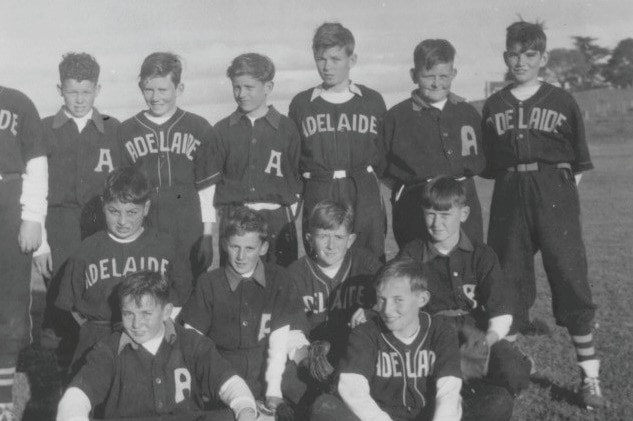 A black and white photo of twelve boys wearing baseball uniforms standing and sitting in three lines