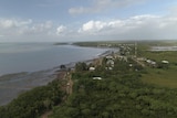 Aerial view of green island, small village, sandy mudflats meets flat tropical sea.