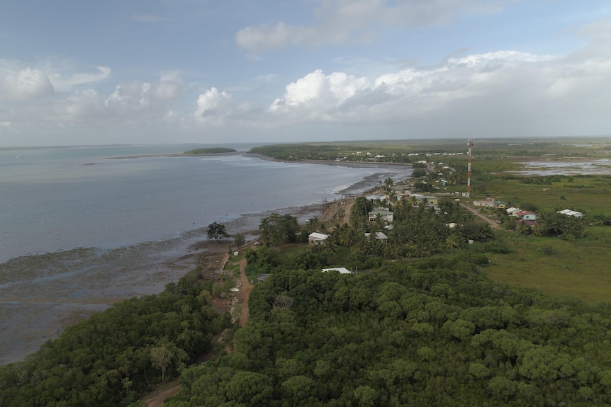 Aerial view of green island, small village, sandy mudflats meets flat tropical sea