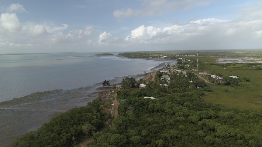 Aerial view of green island, small village, sandy mudflats meets flat tropical sea.
