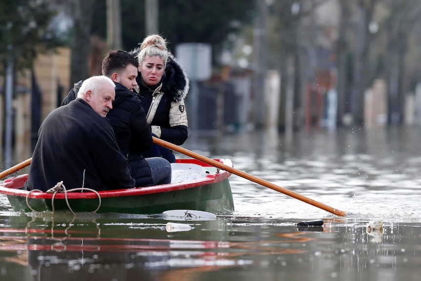 A woman sits in a small boat and cries while two men row it in floodwaters.