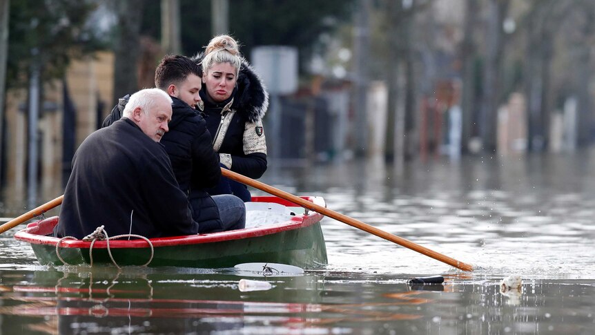 A woman sits in a small boat and cries while two men row it in floodwaters.