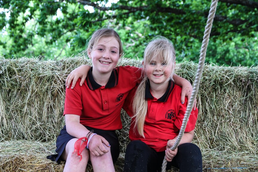 Two young female practitioners of parkour sitting on hay bales with a rope in their hand.