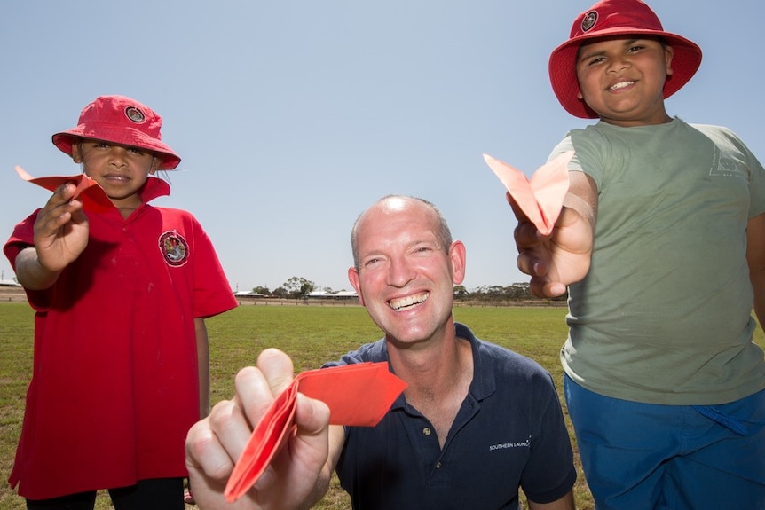 A man and two students hold paper planes.