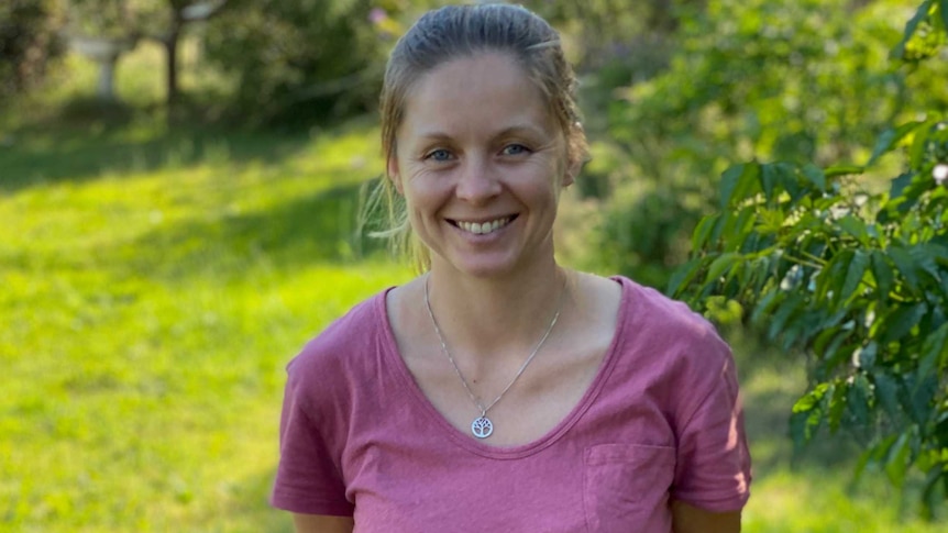 A blonde woman smiles at the camera in a garden.