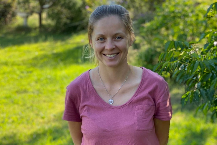 A blonde woman smiles at the camera in a garden.