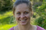 A blonde woman smiles at the camera in a garden.