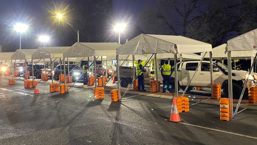 police standing near white tents as cars cue up at border checkpoint