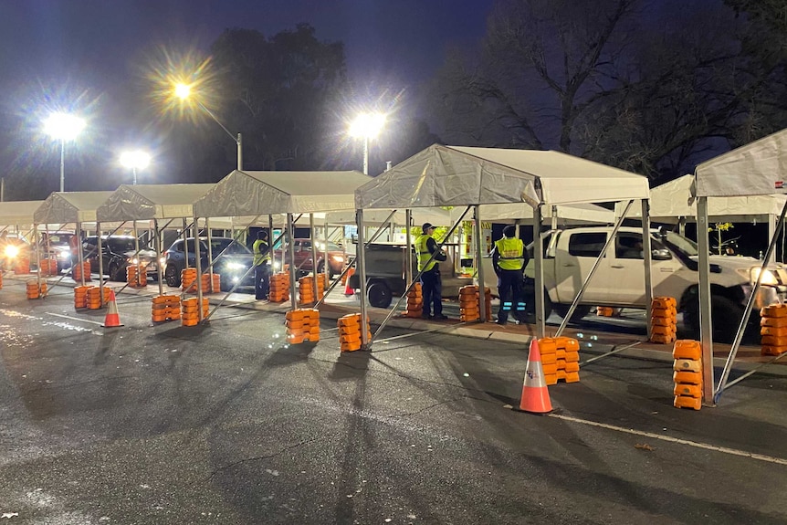 police standing near white tents as cars cue up at border checkpoint