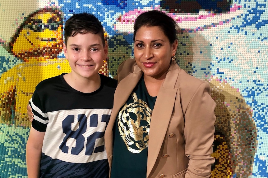 Mum and son standing in front of a Lego wall.