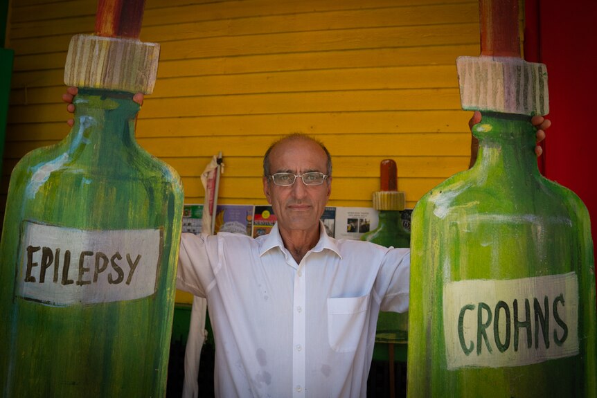 Man holds two large dropper bottles made of cardboard. The left  one is labelled epilepsy and the right one is labelled crohns.